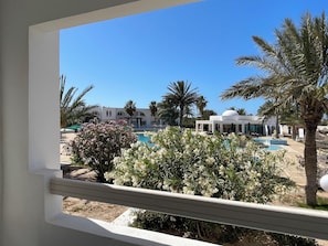 A pool area with palm trees and a building with a dome in the background. - Hotel Bougainvillier Djerba (Djerba Midun)