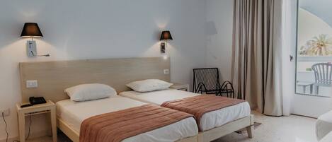 Habitación de hotel con dos camas, lámparas de noche, mesitas de noche, una silla y vistas al exterior.