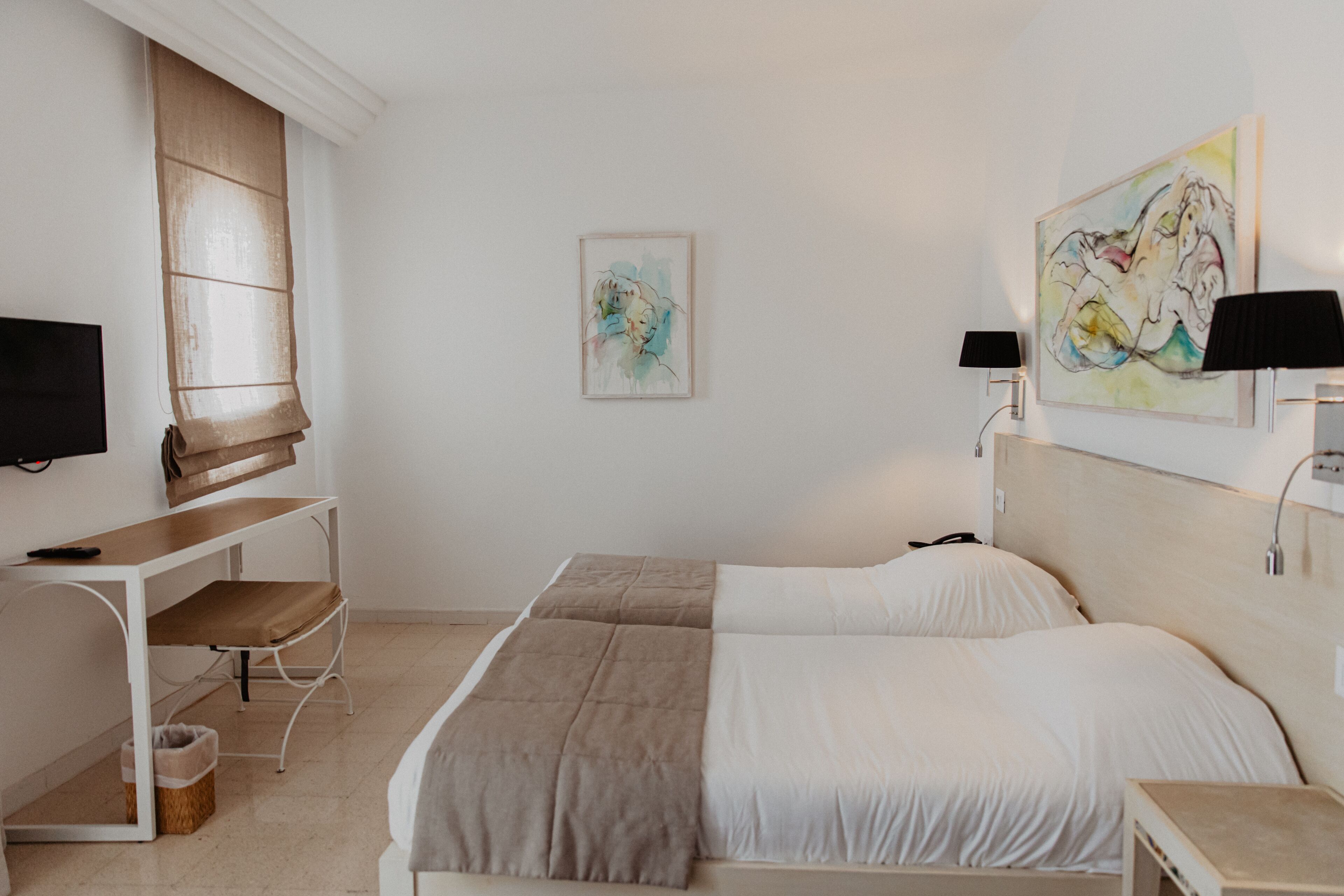 Ein Hotelzimmer mit Bett, Schreibtisch, Stuhl, Fernseher und Kunstwerken an den Wänden.