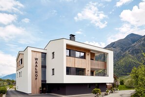 A modern two-story building with a flat roof, large windows, and a visible name 'WALHOF' on the side.
