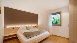 Quarto com cama de madeira, janela com vista para vegetação e prateleira embutida.