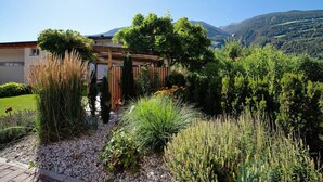 Jardim com pérgola de madeira, plantas diversas e montanhas ao fundo.