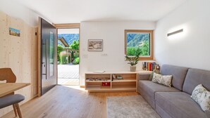 Uma sala de estar moderna com piso de madeira, um sofá cinzento, uma mesa de jantar de madeira e uma estante.