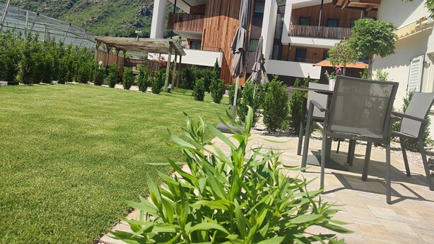 Um edifício moderno com área de estar coberta ao ar livre, um gramado bem cuidado e montanhas ao fundo.