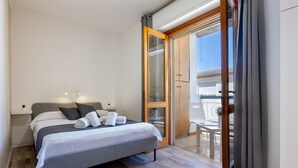 Une chambre à coucher comprenant un lit, une table de chevet, une petite table avec une lampe et une porte-fenêtre coulissante donnant sur un balcon.