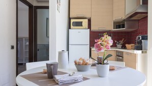 Une cuisine moderne avec un réfrigérateur blanc, un four à micro-ondes et une cuisinière, une table à manger ornée d’une orchidée en pot et un panier de pain.