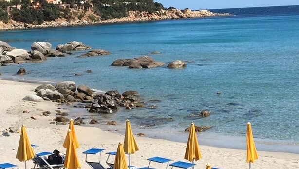 A beach with clear blue water, rocks, and a row of yellow umbrellas and blue lounge chairs. - Holiday Home "Loft Pina" with Wi-Fi, Garden & Terrace (Arbatax)