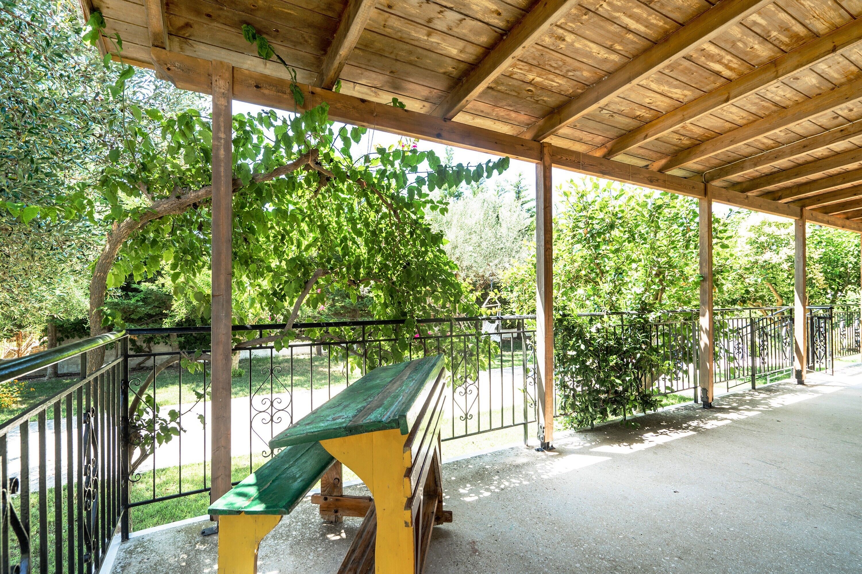 A covered outdoor area with a bench, wooden beams, and a metal fence.