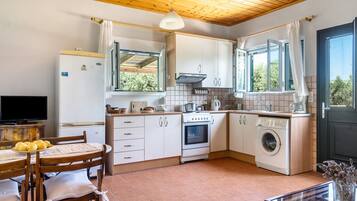 Une cuisine compacte avec un plafond en bois, des armoires blanches, un four encastré, un lave-linge et un coin repas avec une table et des chaises.