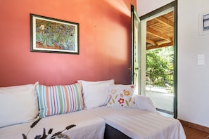 A room with a bed, pillows, a framed artwork, and a view through an open door.