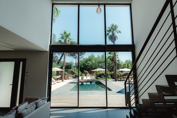 A modern interior with a large glass door leading to an outdoor pool area, wooden deck, and a staircase.