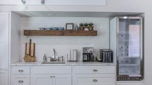 Una cocina con armarios blancos, cafetera integrada, tostadora y refrigerador.
