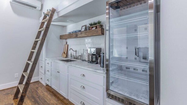 Una cocina con armarios blancos, un refrigerador de acero inoxidable, una escalera de madera y una cafetera.