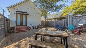 Un patio trasero con una mesa y sillas de madera, una parrilla y una casa con puerta principal y escalones.