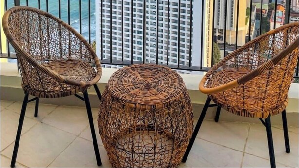 Un balcón con sillas de mimbre y una mesa redonda, con vistas a la ciudad y al mar.