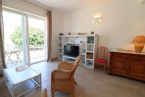 A living room with a television, wicker chairs, a small table, and a wooden cabinet.