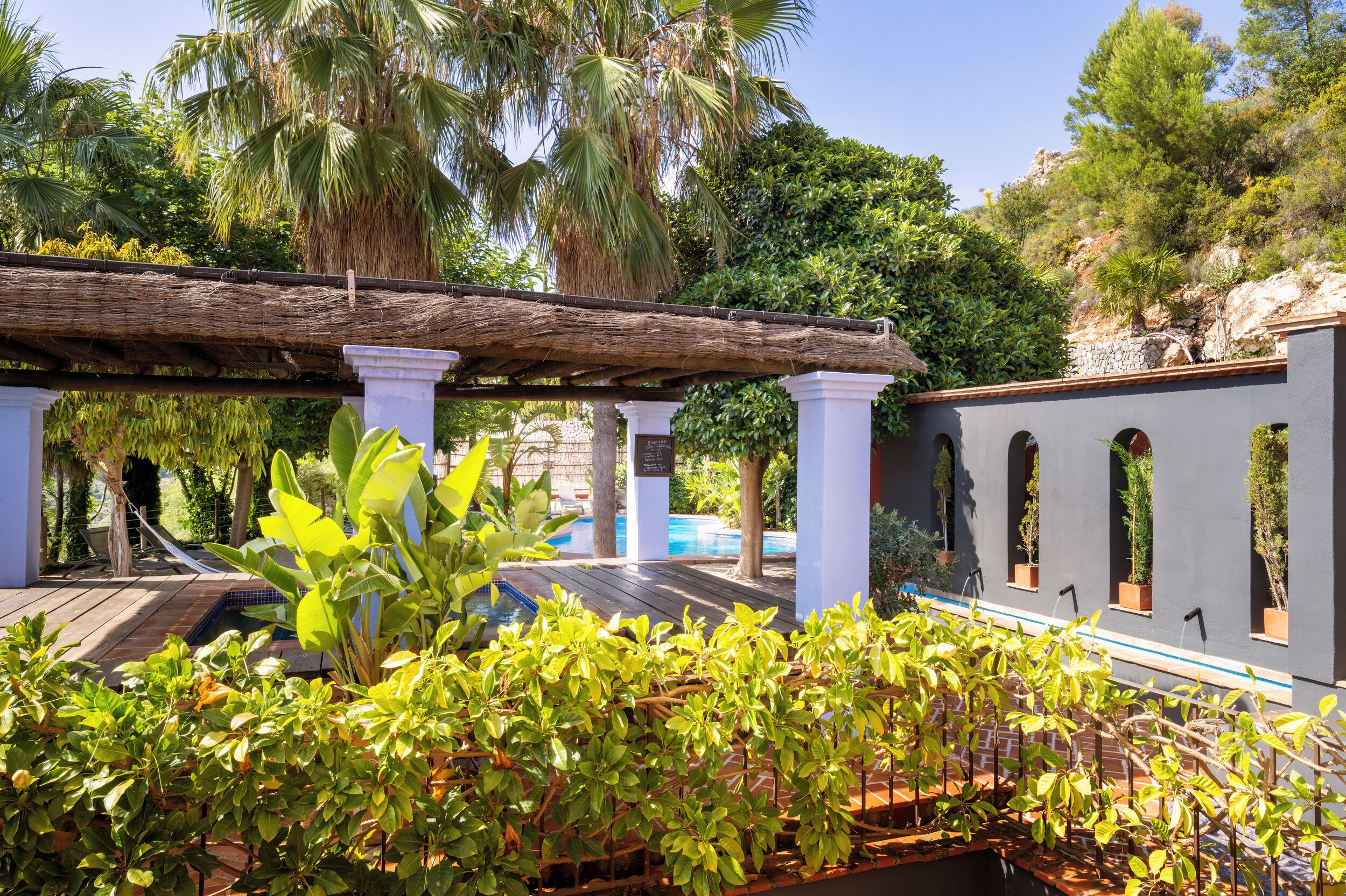 Una terraza de madera con pérgola, plantas en macetas y una zona de piscina.