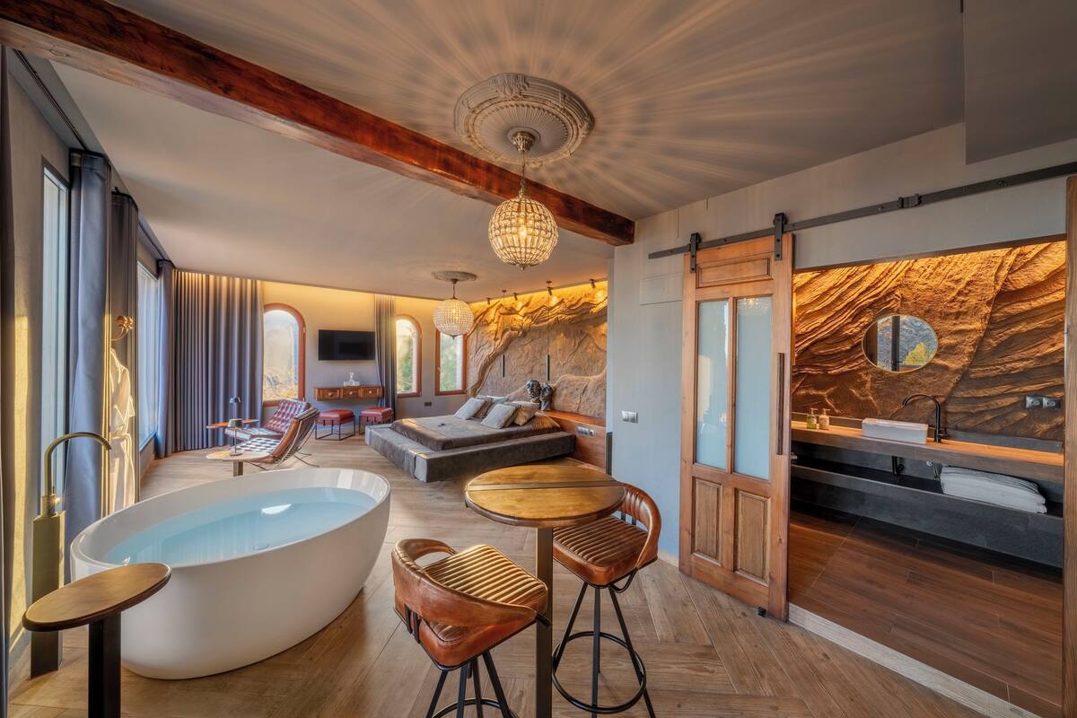 Una habitación amplia con una bañera grande, techo de madera y pared de piedra.