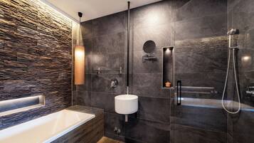 A modern bathroom with a stone wall, a large bathtub, a wall-mounted sink, and a shower.