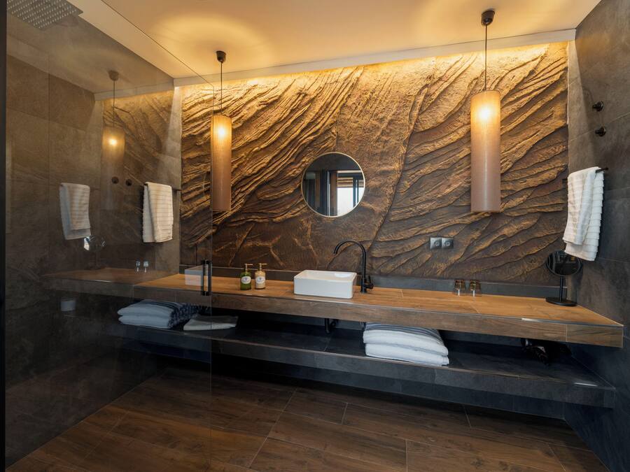 A modern bathroom with a marble wall, a large mirror, and a wooden vanity.
