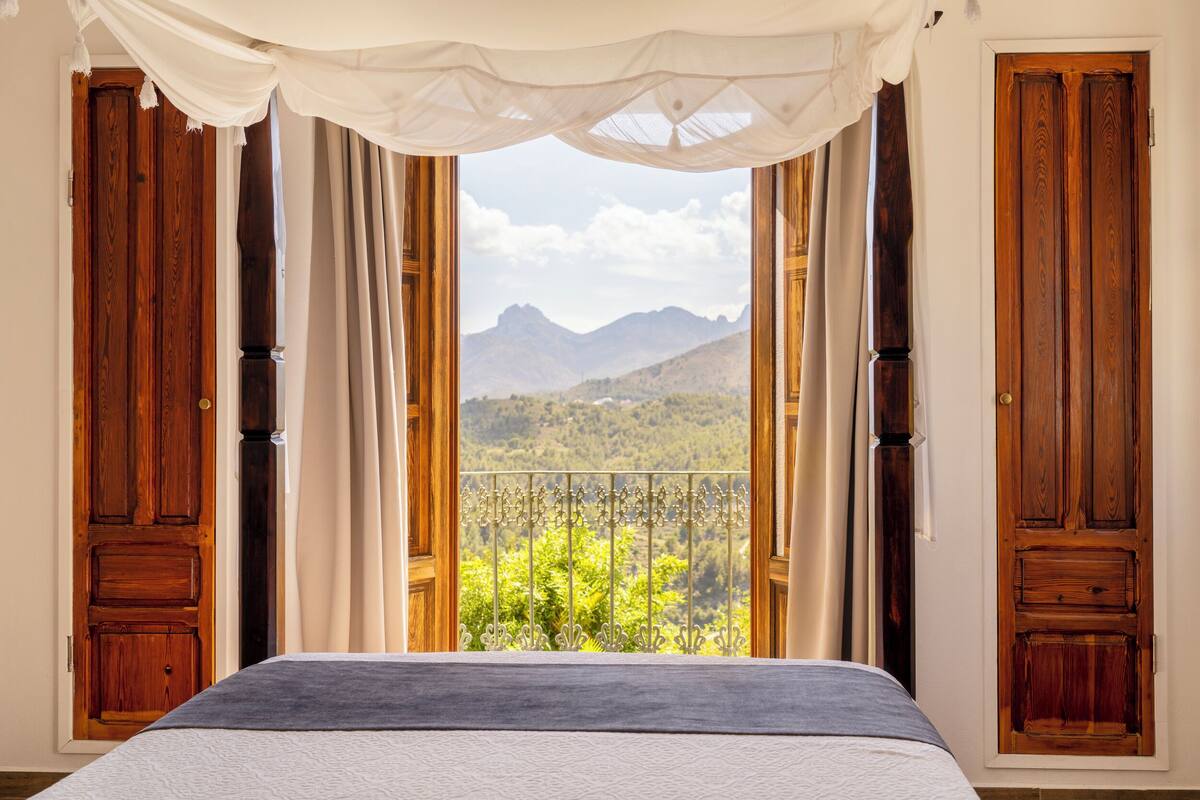 Un dormitorio con una cama, un balcón con vistas a montañas y puertas de madera.