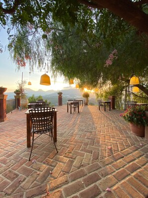 An outdoor patio with brick flooring, tables, chairs, hanging lamps, and potted plants. - Finca el tossal (Bolulla)