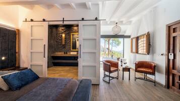 Un dormitorio moderno con cama, escritorio, silla y vistas a un muro de piedra y paisaje exterior.