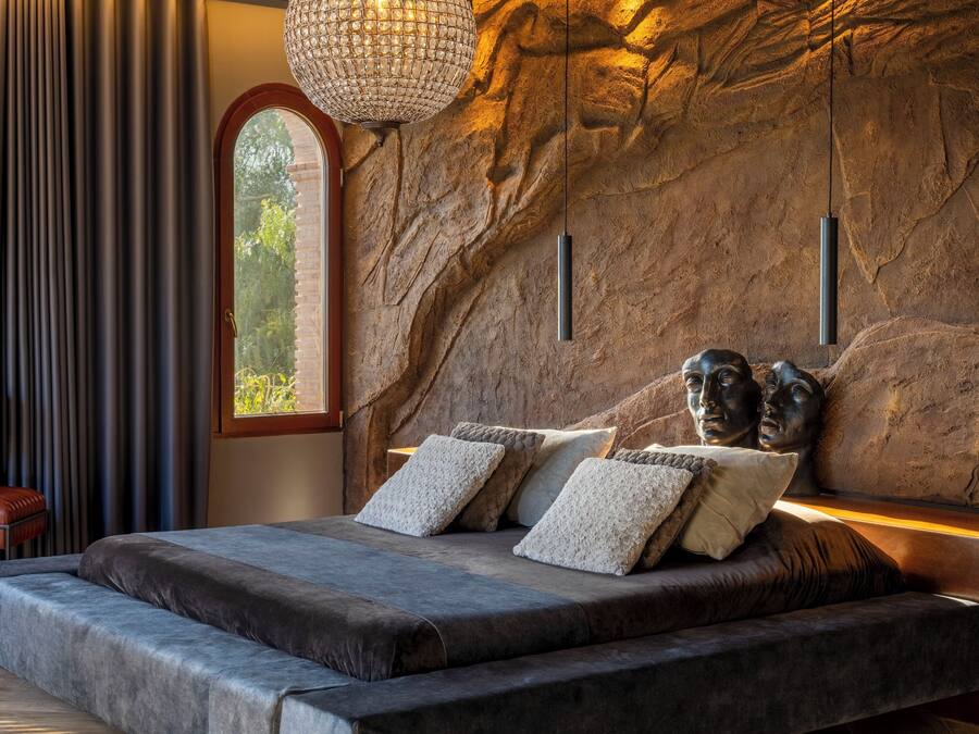 Une chambre avec un grand lit, un mur en pierre, un lustre et une fenêtre.