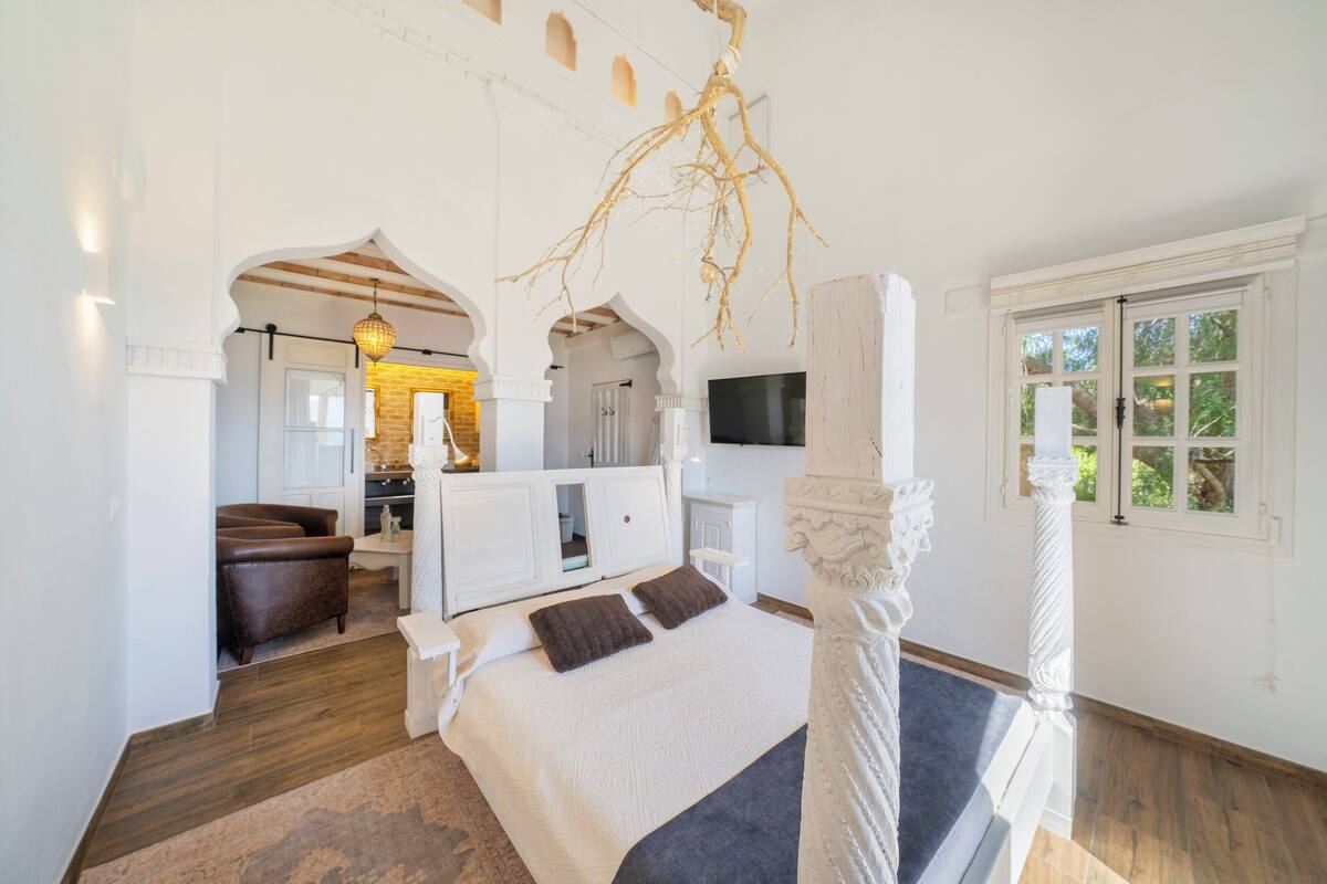Un dormitorio con una cama grande, televisión, candelabro y vistas al exterior.
