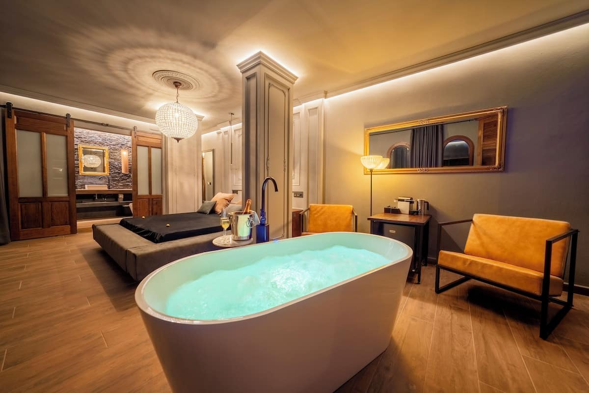 Un moderno spa con una bañera grande, suelo de madera, un sofá y un espejo en la pared.