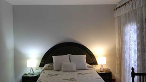 A bedroom with a bed, two bedside lamps, a chair, and a window with curtains.