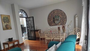 A living room with a teal sofa, a glass coffee table, a dining area with a white table and chairs, and a decorative mirror on the wall.