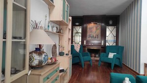 A living room with teal armchairs, a wooden cabinet with glass doors, and a fireplace.