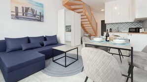 Ein modernes Wohnzimmer mit einem blauen Sofa, einem Esstisch und einer Treppe, die zur Küche führt.