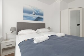 A neatly made bed with white linens and a blue bedspread, a gray headboard, and a wall-mounted painting of a sailboat. - Spacious Apartment in Mielno | Terrace, Grill, 500 m to the Beach (Mielno)