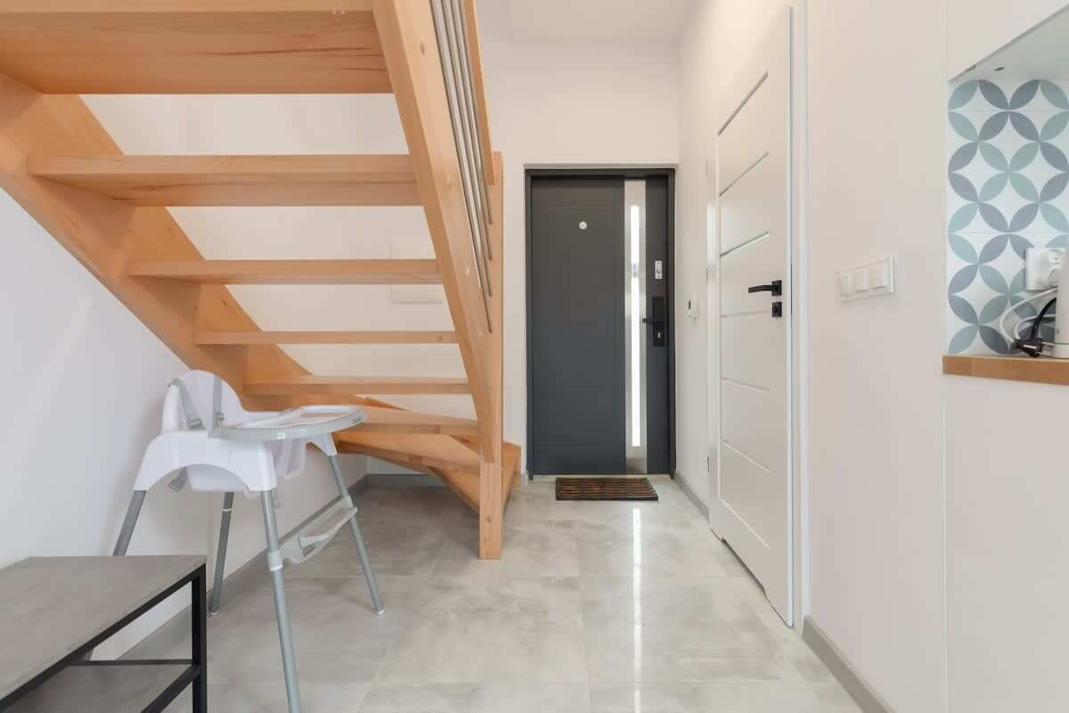 A modern interior with a wooden staircase, a white chair, and a door with a geometric-patterned wall.