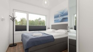 Ein modernes Schlafzimmer mit Bett, einem Fenster mit Jalousien, einem Bild an der Wand und einer Stehlampe.