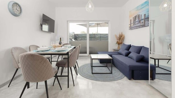Ein modernes Wohnzimmer mit einer Couch, einem Esstisch, Stühlen und einem Fernseher.