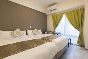 A hotel room with two beds, a small table, a chair, and a window with green curtains. - Mr.KINJO GRAND CATS (Ishigaki)