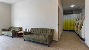 Ein helles, modernes Zimmer mit einer Couch und einem kleinen Tisch, einer Waschgelegenheit mit gelbem Vorhang und einem Fliesenboden.