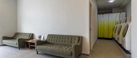 A clean, modern room with a sofa and a small table, a laundry area with a yellow curtain, and a tiled floor.