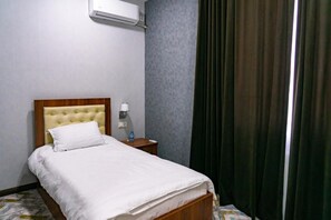 A neatly made bed with a wooden headboard, a bedside table with a lamp, and a wall-mounted air conditioner.