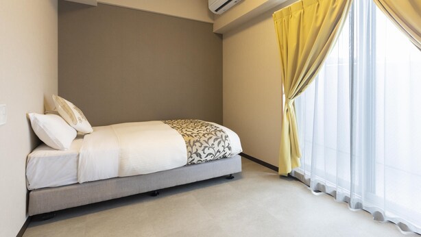 Un dormitorio con cama, ventana con cortinas amarillas y un equipo de aire acondicionado en la pared.