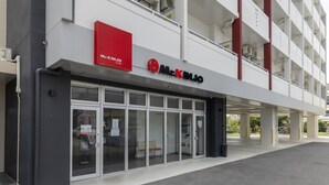 Un edificio moderno con un llamativo letrero del Sr. Kinjo, amplios ventanales y una zona de entrada cubierta.