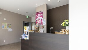 Un área de recepción con un mostrador oscuro, un cartel de bienvenida y un anuncio que ofrece servicio las 24 horas.