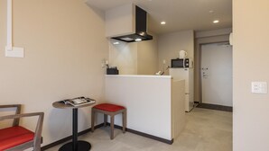 Una cocina compacta con microondas, una mesita con una silla roja y una zona de kitchenette.