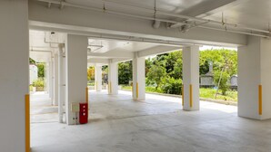 Amplio espacio interior con pilares blancos y suelo de concreto, que incluye una caja roja de emergencia y una vista despejada al exterior con vegetación.