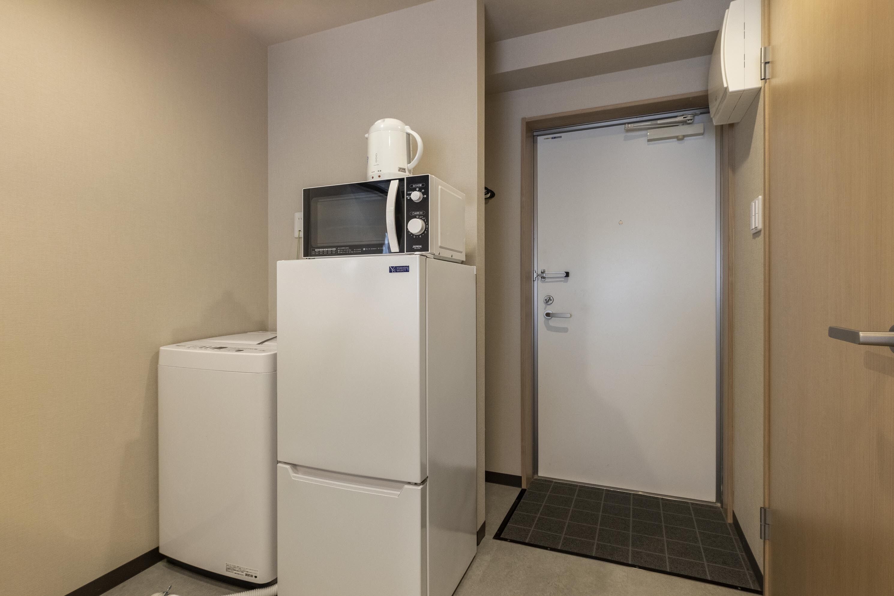 A compact hotel room with a refrigerator, microwave, and a small washing machine.