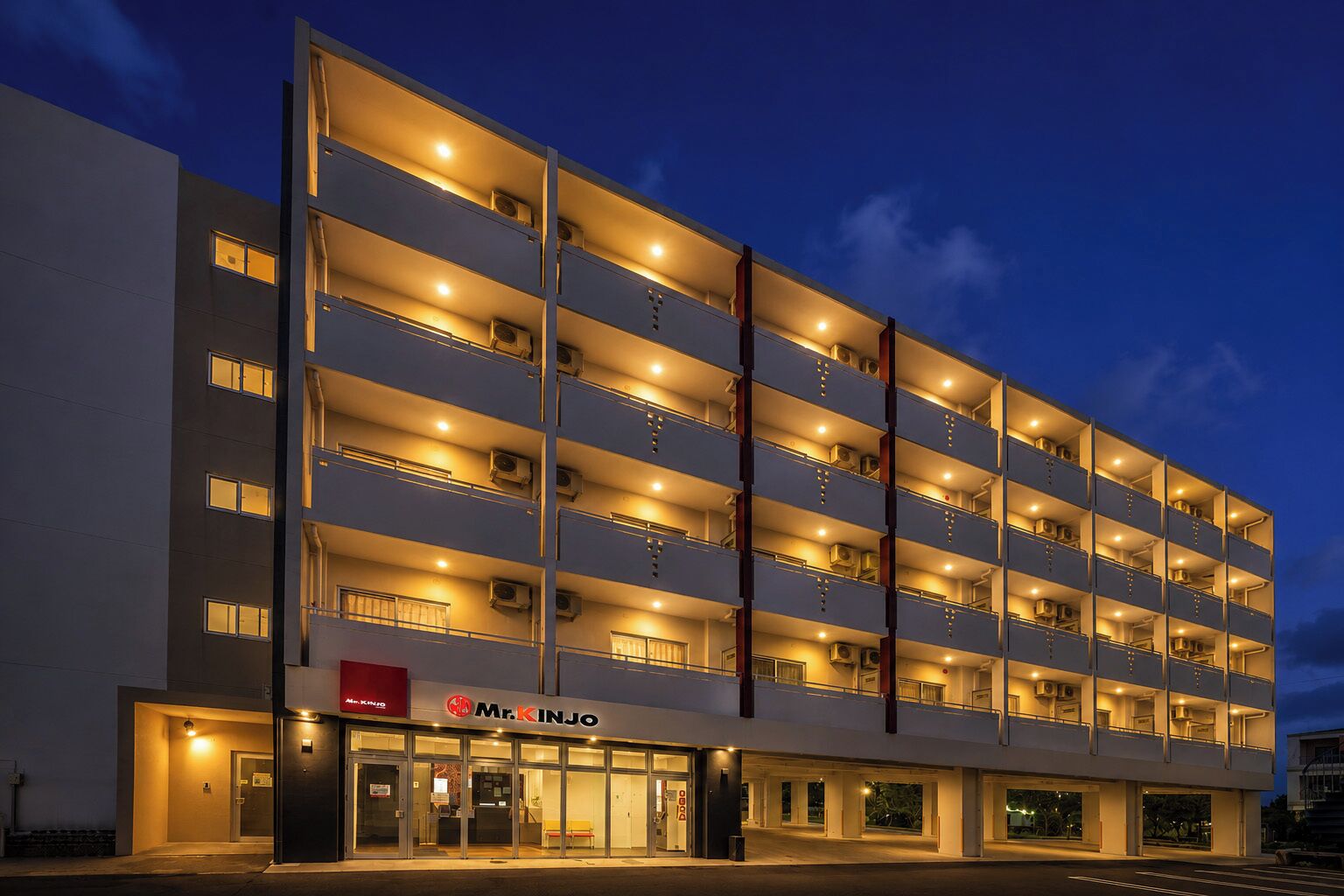 Een meerlaags hotel met een modern ontwerp, met balkons op elke verdieping en een duidelijke ingang met een bord.