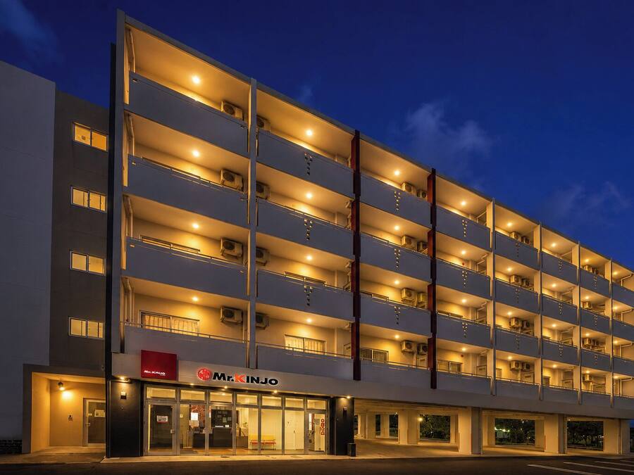 A multi-story hotel with a modern design, featuring balconies on each floor and a visible entrance with a sign.